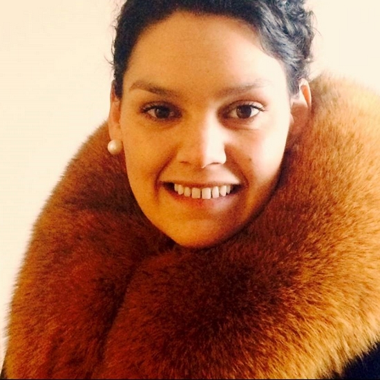 Iimali smiling at the camera wearing pearl earrings and a fur coat.